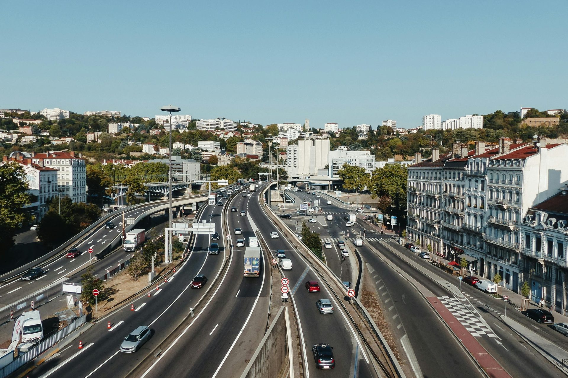From above of asphalt roads with driving vehicles between buildings in living area of town