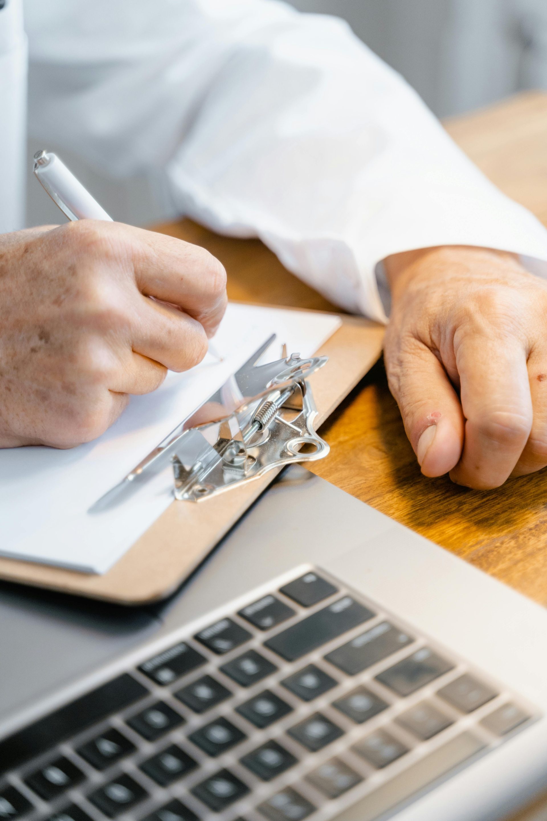 Man writing notes on a clipboard next to a laptop in a professional setting.